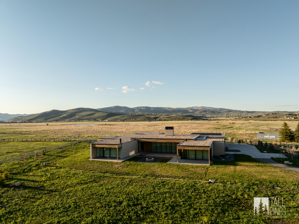 Aerial view of a modern flat-roof mountain home in Park City, Utah, surrounded by open fields and mountain views.