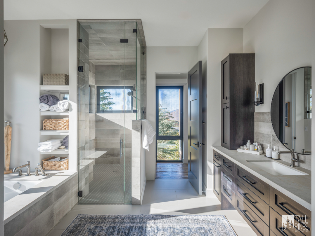 A luxurious bathroom featuring a frameless glass shower, soaking tub, built-in shelving, and a window showcasing surrounding trees.