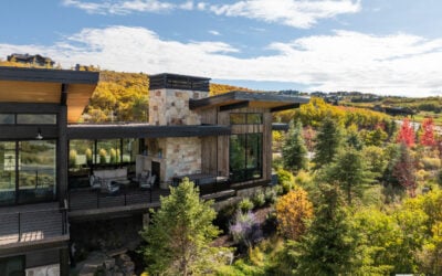 A luxury mountain home featuring floor-to-ceiling windows, natural stone accents, and vibrant fall foliage.