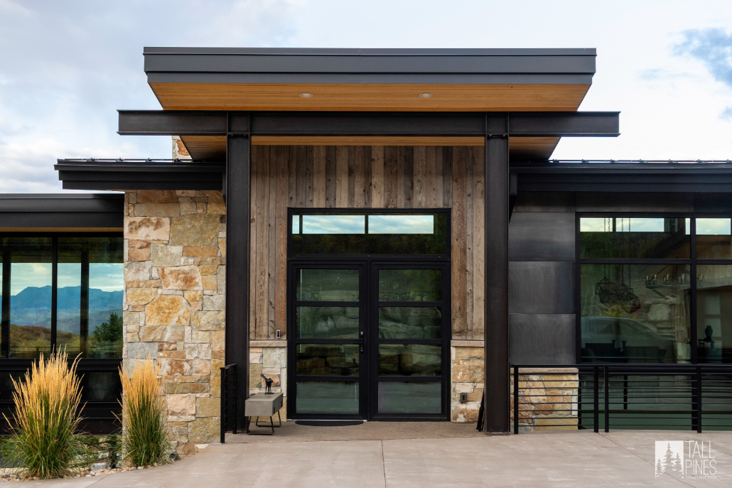A close-up exterior entry with stone and wood cladding, modern black-framed windows, and a covered porch.
