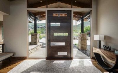 A Mountain Modern entryway featuring a custom wood front door, natural stone, and expansive glass that connects the interior to the surrounding Park City landscape, showcasing Tall Pines Construction’s craftsmanship.