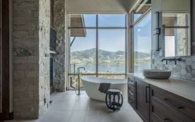 Freestanding soaking tub in a custom bathroom with large windows framing scenic mountain and lake views.