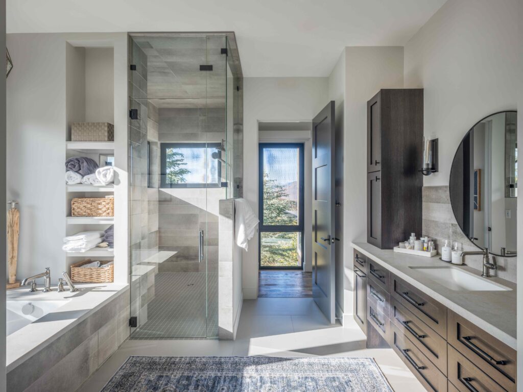 Luxury custom bathroom with a wood vanity, frameless glass shower, built-in storage, and bright natural light.