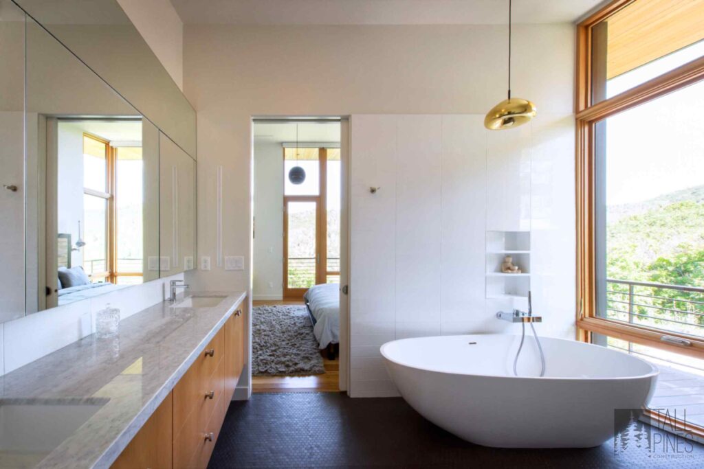 Modern custom bathroom with a freestanding tub, warm wood vanity, oversized window, and clean spa-inspired finishes.