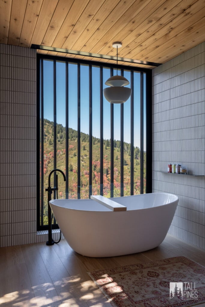 Freestanding soaker tub positioned beside a floor-to-ceiling window with a peaceful Utah mountain view.