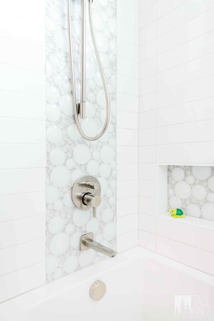 Bright spa-inspired shower with white tile, decorative mosaic accents, and a built-in storage niche.