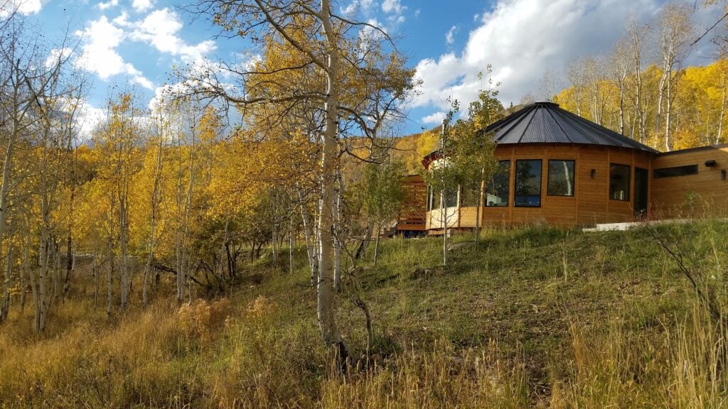 Exterior view of a luxury Park City yurt surrounded by vibrant autumn aspens, blending modern architecture with the natural landscape.