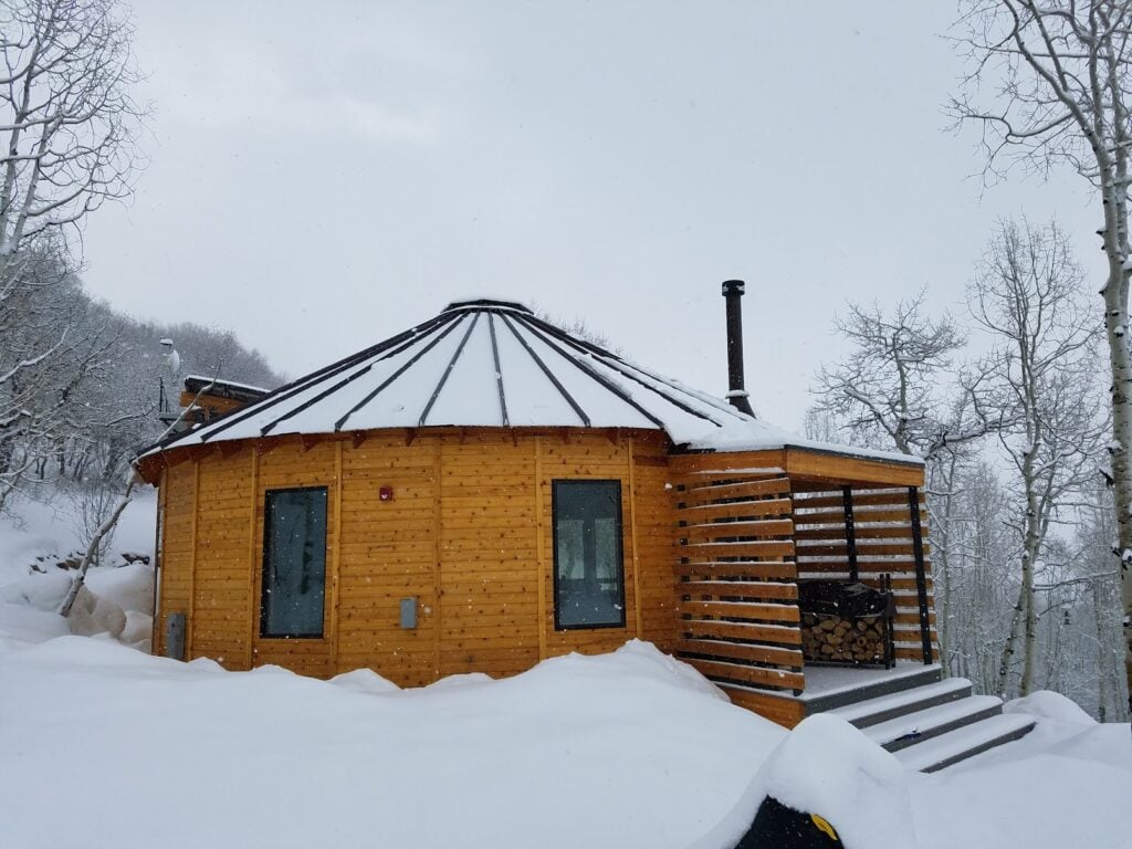 Exterior of a custom Park City yurt in winter with a snow-covered roof, demonstrating year-round mountain living and luxury design.
