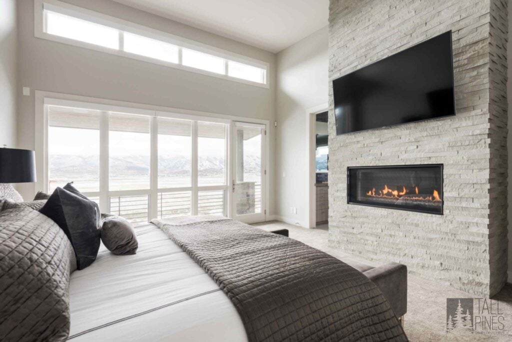 Luxury primary bedroom in a Park City custom home featuring a stone fireplace, expansive windows, and mountain views.