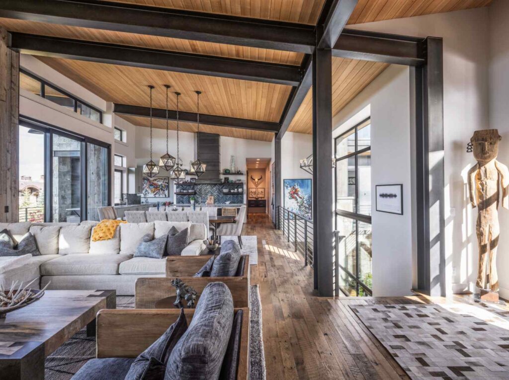 Open-concept mountain home interior featuring exposed steel beams, wood ceilings, expansive windows, and luxury living spaces.