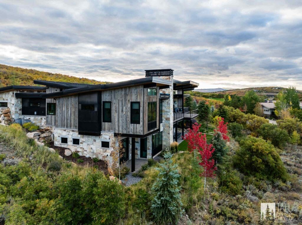 Modern custom mountain home in Park City featuring stone, wood siding, and expansive windows.