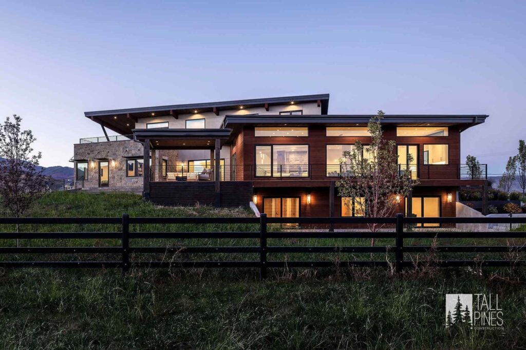 Exterior of a mountain modern custom home in Utah featuring wood, stone, expansive windows, and contemporary rooflines.