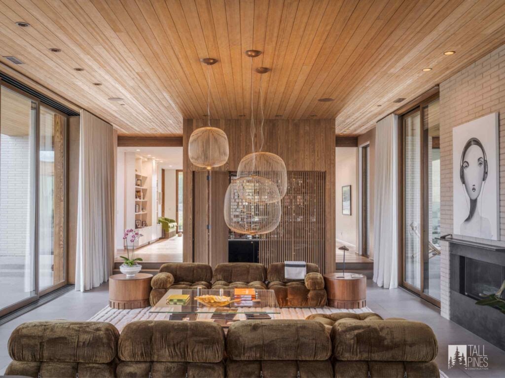Open mountain modern living room featuring natural wood, contemporary lighting, large windows, and a fireplace.