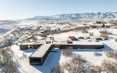 Aerial view of a custom home construction project surrounded by snow-covered Utah mountain terrain.