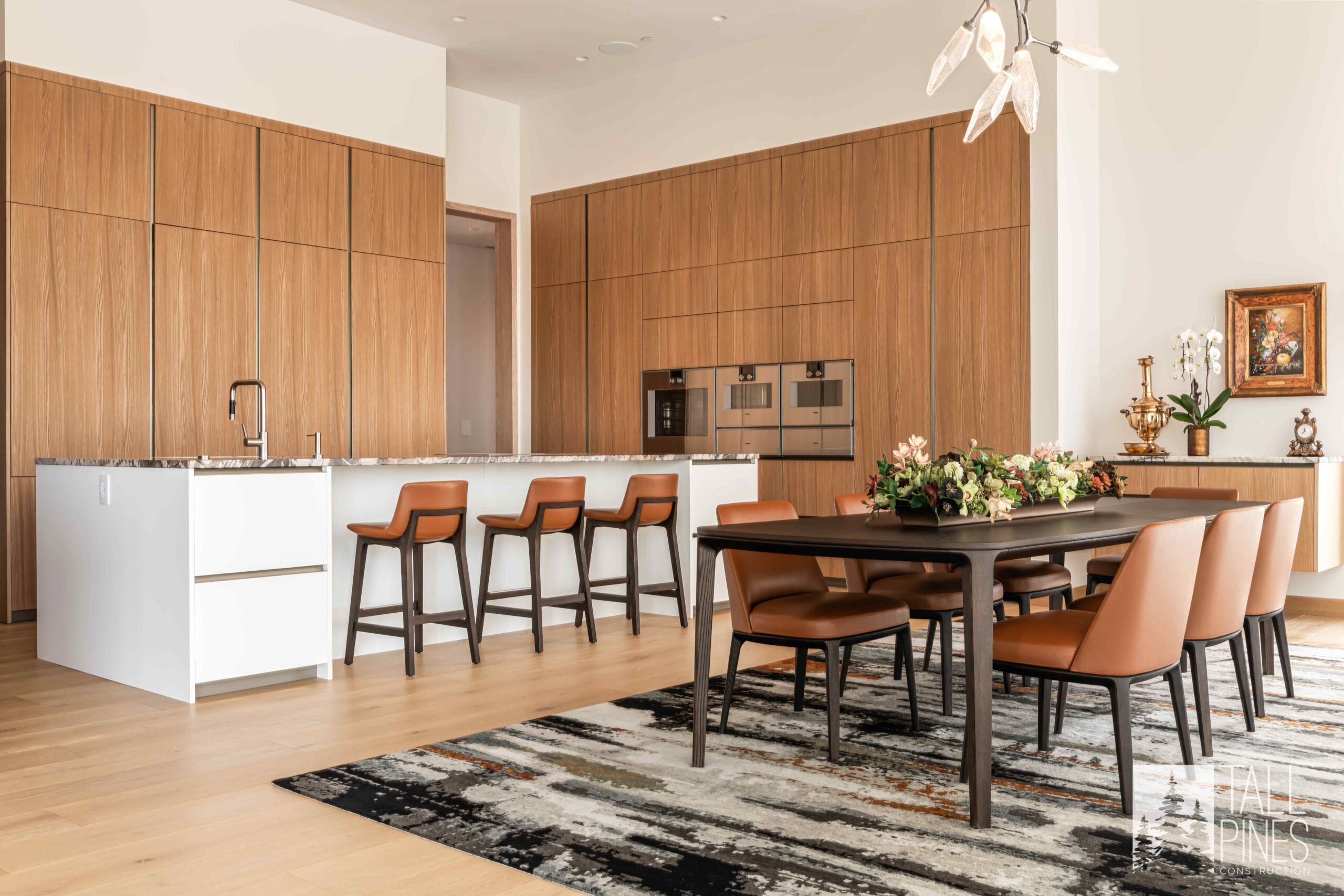 Open kitchen and dining area at Ridgeline Light with warm wood cabinetry, white island, leather seating and contemporary lighting.